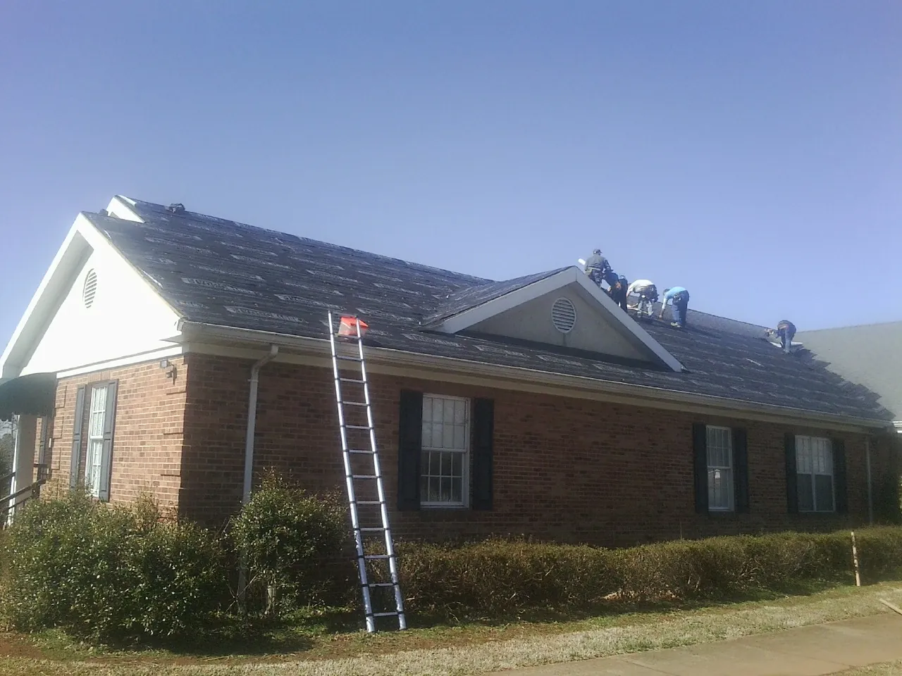 Crew tearing shingles off a brick ranch roof with a ladder set — Metal Roof Repair work by our crew in Christiansburg