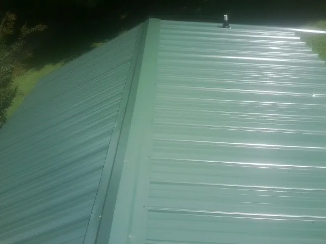 New green metal panels meeting at the ridge of a roof — Flat Roof Repair work by our crew in Christiansburg